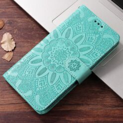 Teal embossed phone wallet case with a mandala pattern placed on a laptop on a wooden desk. | Levné Kryty