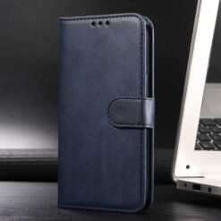 Navy blue leather flip wallet phone case with a magnetic strap standing upright beside a laptop on a desk